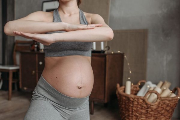 Fit pregnant woman doing yoga indoors, focusing on health and flexibility.