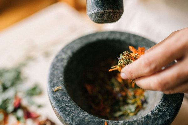 Close-up of hands using a stone mortar to grind colorful herbs for culinary or medicinal use.
