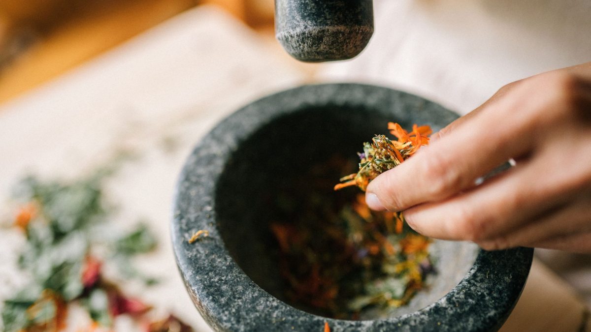 Close-up of hands using a stone mortar to grind colorful herbs for culinary or medicinal use.
